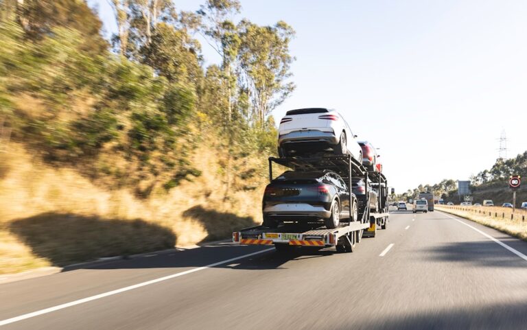 A vehicle being loaded onto an open auto transport trailer with a driver nearby.