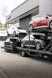 A large car carrier truck parked on a suburban street as cars are loaded for transport.