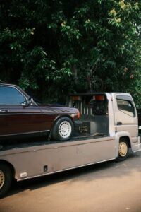 A person and driver inspect a car together before loading it onto a large auto transport truck on a residential street.