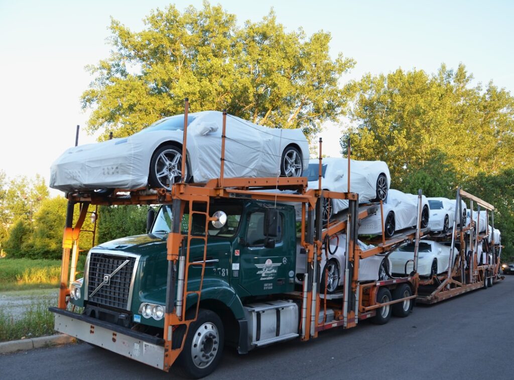 A car carrier truck loading vehicles on a residential street with trees and houses in the background.