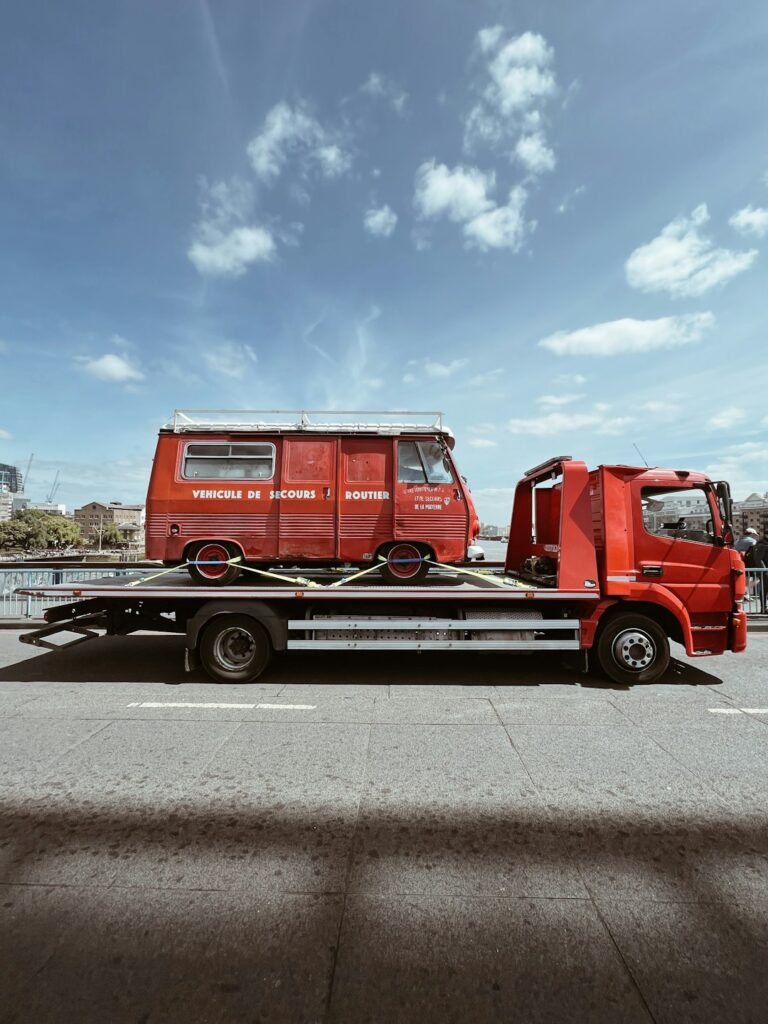 A car being loaded onto an open vehicle transport carrier in a suburban residential neighborhood.