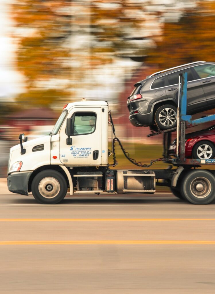 A technician secures a sedan’s tires with straps on a vehicle transport trailer.