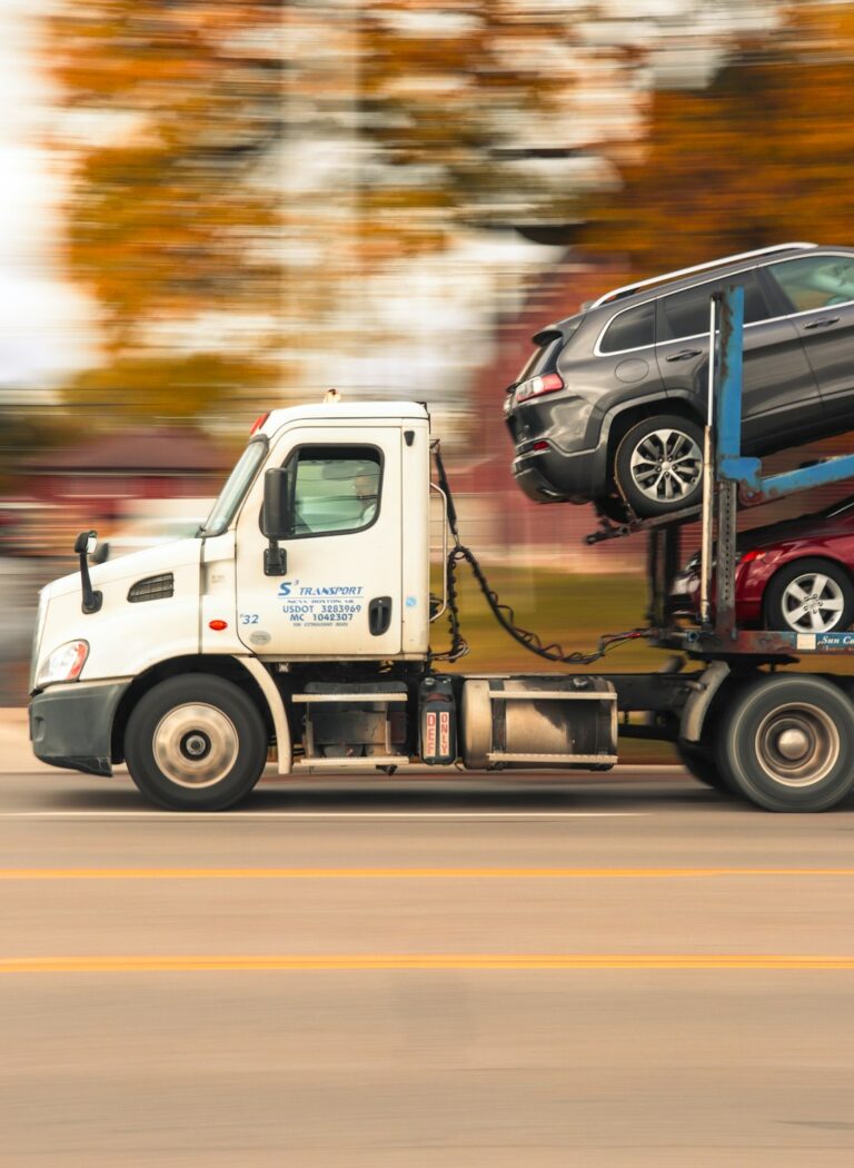 A technician secures a sedan’s tires with straps on a vehicle transport trailer.